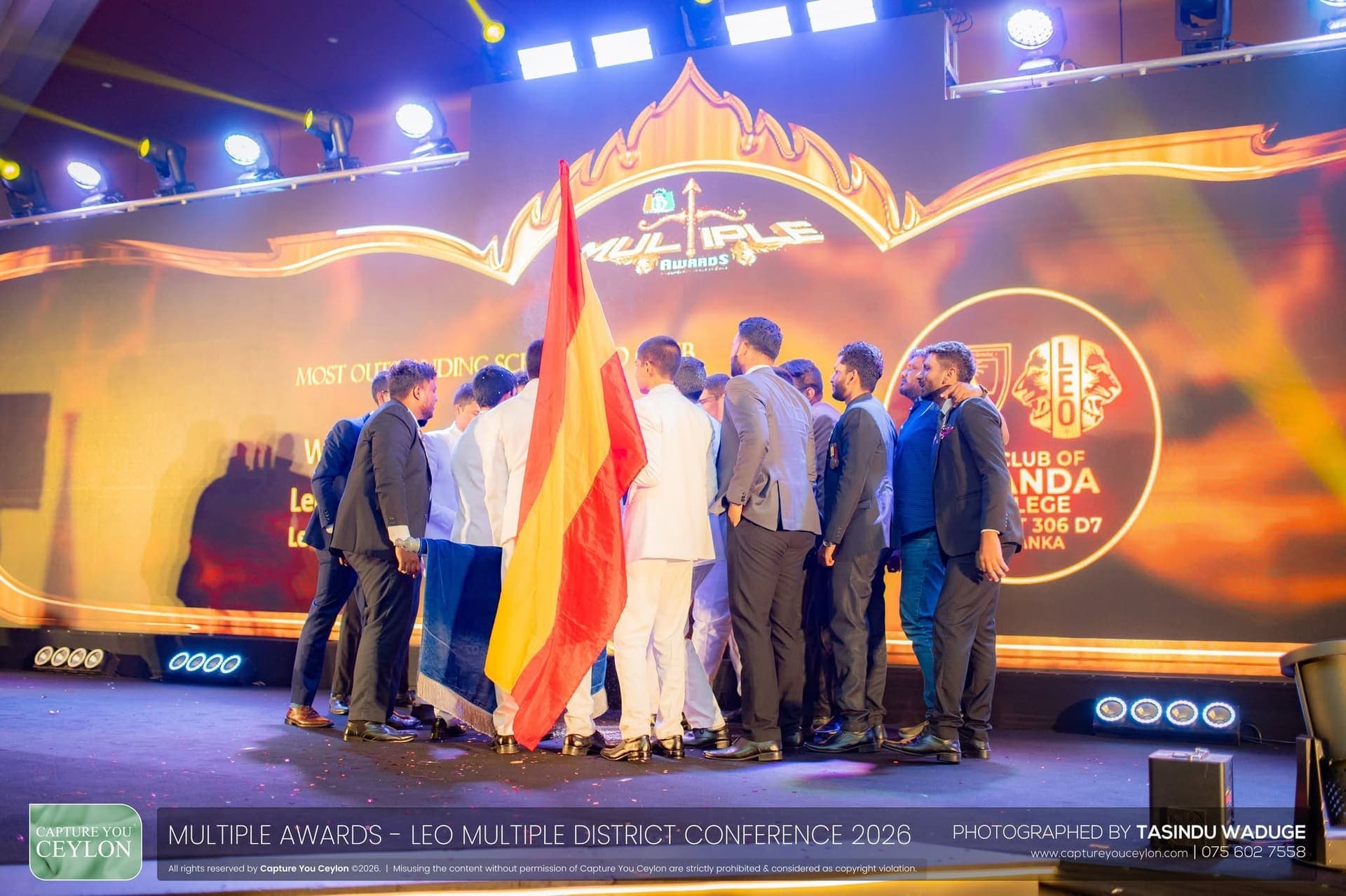 Members gathered on the Multiple District stage under the Most Outstanding School Leo Club title screen, the maroon and gold Ananda flag raised among them